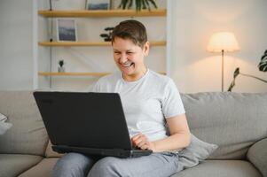 Elderly female sit on couch holding on lap laptop search information, check or typing e-mail, spend time on-line, modern tech, easy interesting pastimes services for retired older generation concept. photo