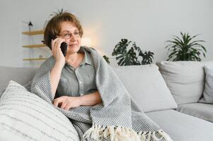 bella anciana con ropa informal usando su teléfono inteligente mientras se sienta en el sofá de casa foto