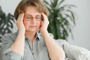 An elderly woman has headaches, she touches her head with her hands, reports symptoms of dizziness, migraines. photo