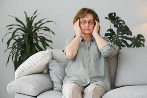 An elderly woman has headaches, she touches her head with her hands, reports symptoms of dizziness, migraines. photo