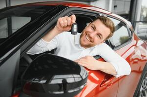 Sí, eso es mi nuevo coche. cliente en coche concesión. joven hombre con llaves en mano. foto