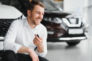 Happy buyer holding keys near the car in front of the modern avtosalon building photo