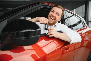 Yes, that's my new car. Customer in car dealership. Young man with keys in hand. photo