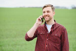 Young handsome farmer walking on farmland, and talking on cell phone photo