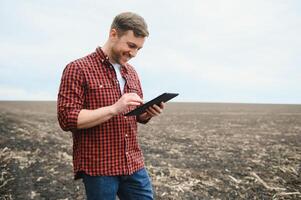 A farmer in boots works with his tablet in a field sown in spring. An agronomist walks the earth, assessing a plowed field in autumn. Agriculture. Smart farming technologies photo