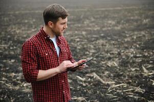 A farmer in boots works with his tablet in a field sown in spring. An agronomist walks the earth, assessing a plowed field in autumn. Agriculture. Smart farming technologies photo