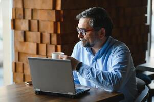 negocio, tecnología y personas concepto , mayor empresario con ordenador portátil computadora Bebiendo café a moderno cafetería. foto