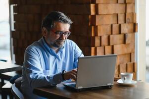 Male freelancer is working in a cafe on a new business project. Sits at a large window at the table. Looks at a laptop screen with a cup of coffee photo