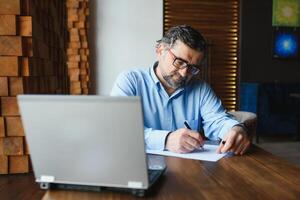 Male freelancer is working in a cafe on a new business project. Sits at a large window at the table. Looks at a laptop screen with a cup of coffee photo