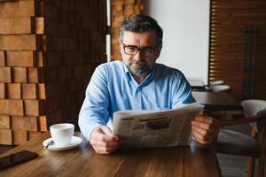 activo mayor hombre leyendo periódico y Bebiendo café en restaurante foto