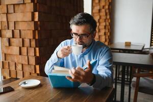 mayor antiguo hombre leyendo un libro en un café comercio, disfrutando su literario pasatiempo foto