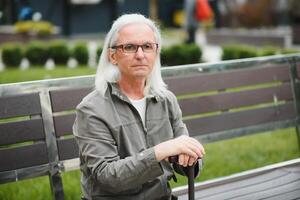 Portrait of senior man holding walking stick while resting in park. photo