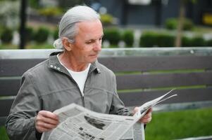 Portrait of senior man reading on bench during summer day. photo