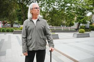 Portrait of senior man holding walking stick while resting in park. photo