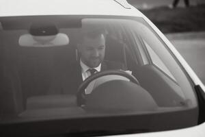 Man of style and status. Handsome young man in full suit smiling while driving a car photo