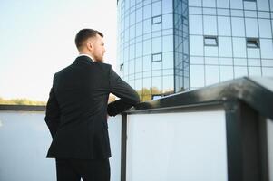 Modern businessman. Confident young man in full suit and looking away while standing outdoors with cityscape in the background photo