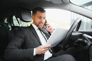 hombre de estilo y estatus. un joven apuesto con traje completo sonriendo mientras conduce un auto foto