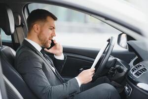 Man of style and status. Handsome young man in full suit smiling while driving a car photo