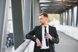 Close up serious businessman drinking take away coffee at street. Portrait of business man waiting with coffee to go outdoor. Office employee looking away at street. Male professional take break photo