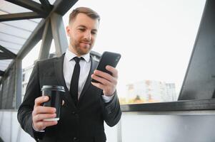 Confident young businessman using cell phone and drinking coffee in the city photo