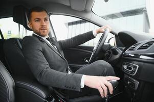 siempre en un apuro. hermoso joven hombre en lleno traje sonriente mientras conducción un coche. foto