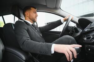 hombre de estilo y estatus. un joven apuesto con traje completo sonriendo mientras conduce un auto foto