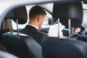 siempre en un apuro. hermoso joven hombre en lleno traje sonriente mientras conducción un coche. foto