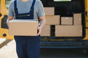 delivery service employee. Portrait of man working in delivery service. Portrait of courier with box. Courier next to minivan. Delivery service career. photo