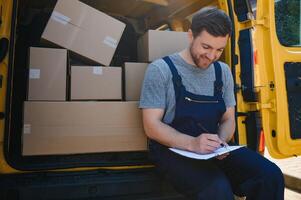 joven entrega hombre mensajero en uniforme sostener documentos portapapeles comprobación lista paquete o empaquetar enviar cajas cerca un coche para Servicio envío a cliente, en línea compras Servicio conceptos. foto