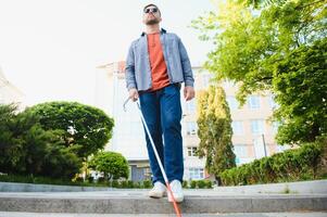 joven ciego hombre con blanco caña caminando a través de el calle en ciudad foto