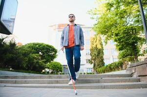 joven ciego hombre con blanco caña caminando a través de el calle en ciudad foto