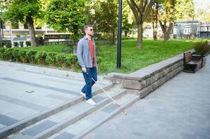 joven ciego hombre con blanco caña caminando a través de el calle en ciudad foto