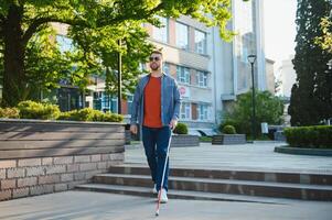 Young handsome blinded man walking with stick in town photo