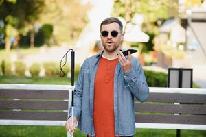 Young blinded man using phone and sending voice message photo