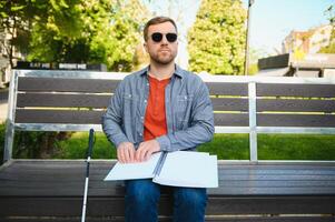 Blind man reading braille book, sitting on bench in summer park, resting photo