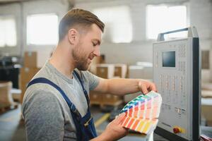 Portrait of production line worker controlling manufacturing process of modern packaging industrial machine in printing factory photo