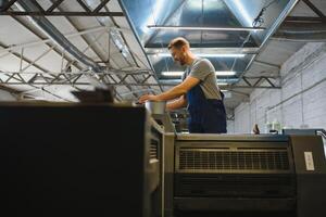 Portrait of production line worker controlling manufacturing process of modern packaging industrial machine in printing factory photo