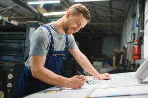 Portrait of production line worker controlling manufacturing process of modern packaging industrial machine in printing factory photo