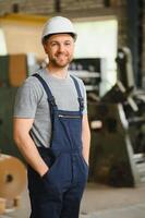 Smiling and happy employee. Industrial worker indoors in factory. Young technician with white hard hat. photo