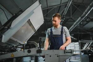 Portrait of production line worker controlling manufacturing process of modern packaging industrial machine in printing factory photo