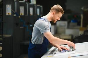 Man worker measuring printing color with spectrometer on the operating desk of the printing plant photo