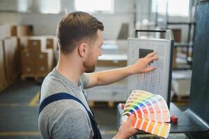 Portrait of production line worker controlling manufacturing process of modern packaging industrial machine in printing factory photo