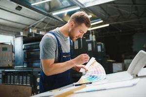 Man worker measuring printing color with spectrometer on the operating desk of the printing plant photo