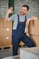 retrato de contento masculino trabajador en almacén en pie Entre estantes. foto