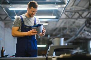 Portrait of production line worker controlling manufacturing process of modern packaging industrial machine in printing factory photo