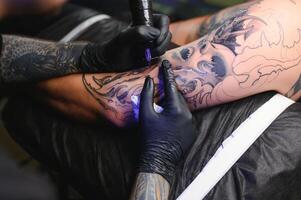 masculino tatuaje artista participación un tatuaje pistola, demostración un proceso de haciendo tatuajes en un masculino tatuado del modelo brazo foto