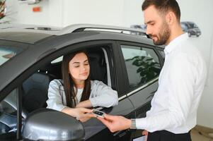 satisfecho contento caucásico hembra cliente cliente mujer sentado a el rueda de nuevo coche mientras masculino tienda asistente Ayudar su escoger eso foto