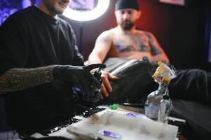 tatuaje artista demuestra el proceso de consiguiendo negro tatuaje con pintar. Maestro trabajos en negro estéril guantes foto