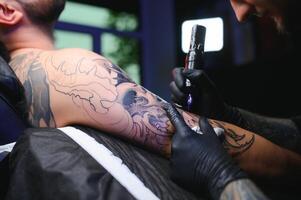 masculino tatuaje artista participación un tatuaje pistola, demostración un proceso de haciendo tatuajes en un masculino tatuado del modelo brazo foto