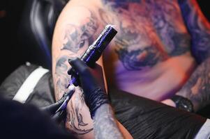 tattoo artist demonstrates the process of getting black tattoo with paint. Master works in black sterile gloves photo